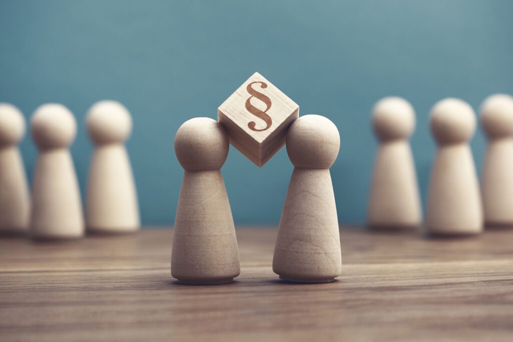 Central wooden pawn holding a small cube with a paragraph symbol, surrounded by other pawns, symbolizing law or legal decision-making